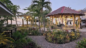 A gazebo with a thatched roof, surrounded by tropical plants and a gravel path. - Vhora Resort (Cajidiocan)