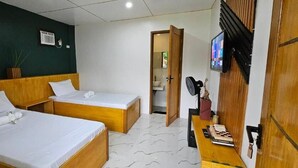 A room with two beds, a wooden headboard, a small table with a book, a TV mounted on the wall, and a door leading to a bathroom. - Vhora Resort (Cajidiocan)