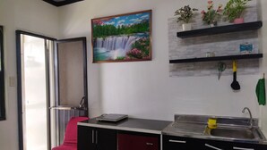 A kitchen with a waterfall painting, a sink, and a chair with a red cushion. - 1_Las Asturias Charming Condo Just Steps from Enchanted Kingdom (CITY OF SANTA ROSA)