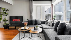 A modern living room with a sectional sofa, a flat-screen TV, a coffee table, and a potted plant. - THE VELVET (Asahikawa)