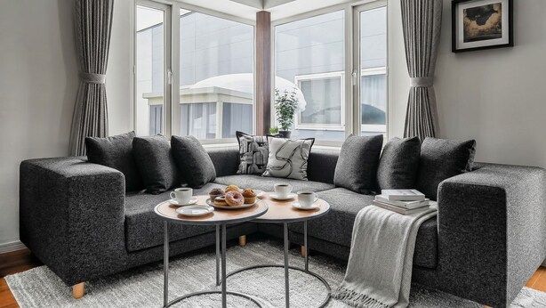 A corner living room with a grey sofa, two small round tables, and a large window with curtains. - THE VELVET (Asahikawa)