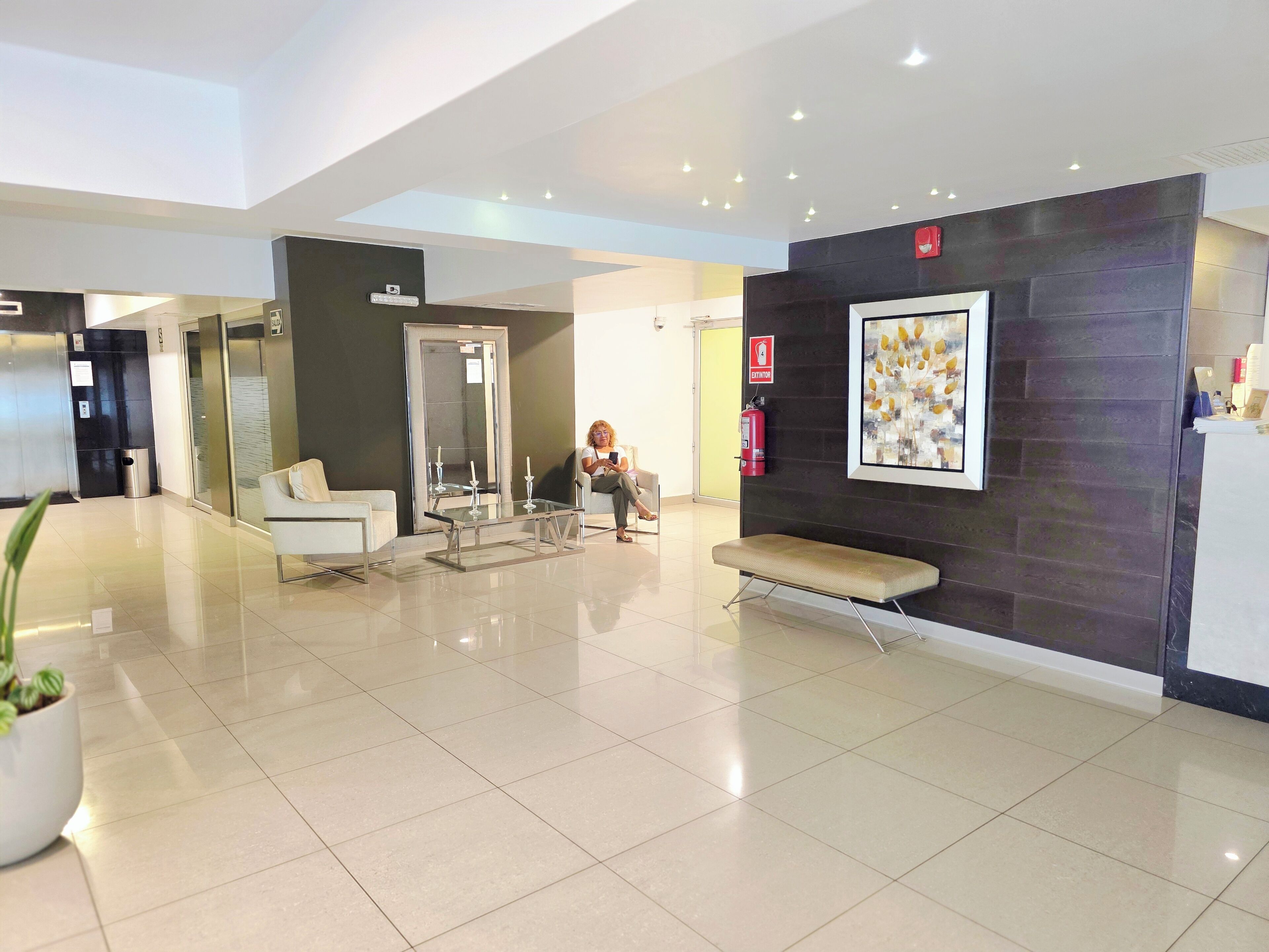 A modern lobby with a glass coffee table, seating area, and a fire extinguisher.