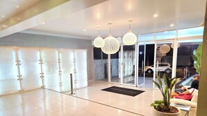Een hotel lobby met een modern ontwerp, met een receptiebalie, een potplant en een glazen deur.