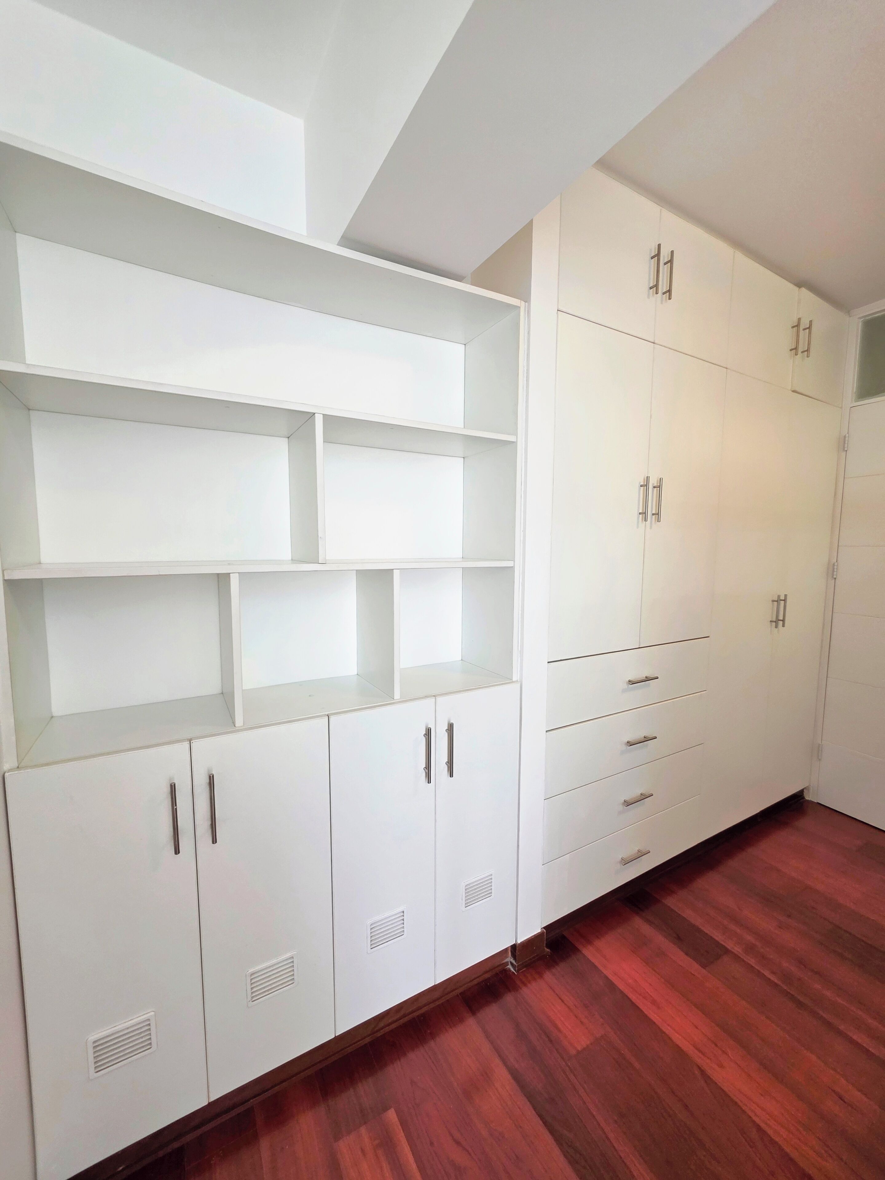 A room with white cabinetry, multiple shelves, and a wooden floor.