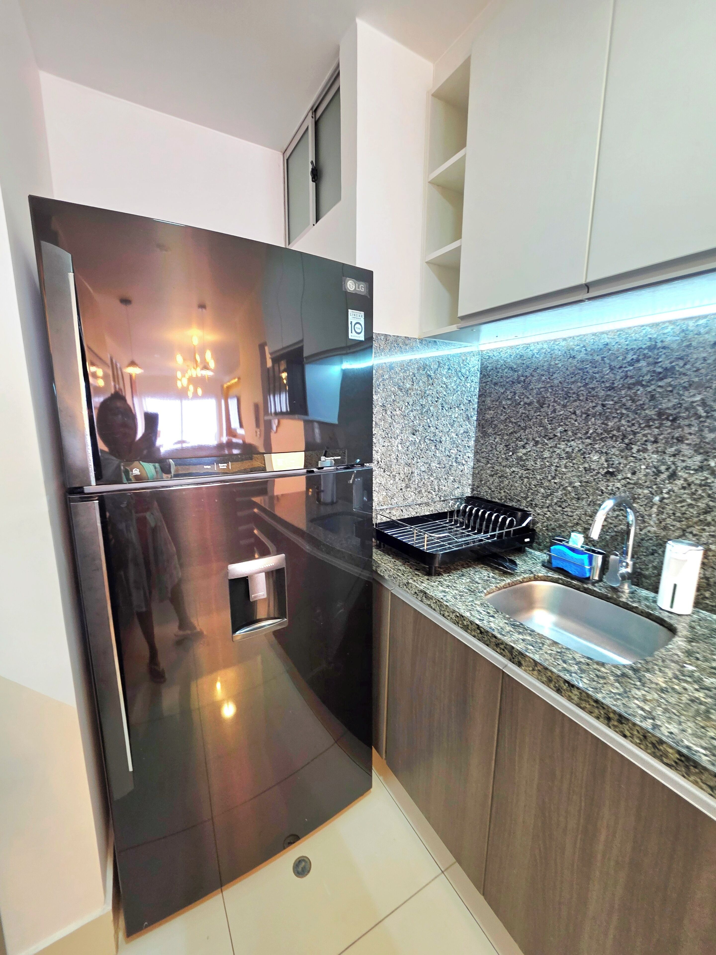 Una cocina moderna con refrigerador de acero inoxidable, encimera de granito y lavamanos integrado.