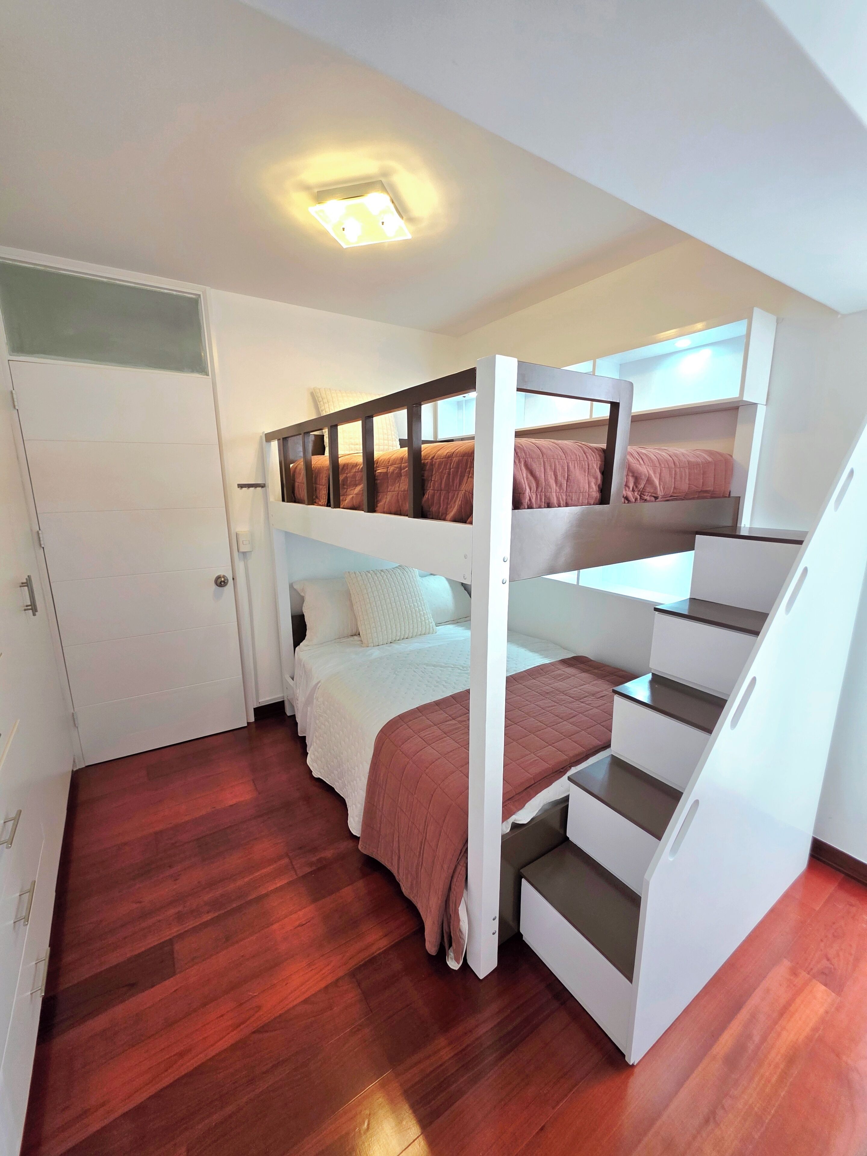 A room with a bunk bed, a staircase, a door, and a ceiling light fixture.