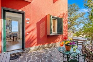 Un bâtiment rouge comprenant un espace repas, une terrasse avec une table et des chaises, et une fenêtre avec des volets.
