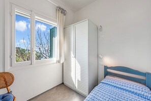 Ein Schlafzimmer mit Bett, einem Fenster mit Rollläden, einem Kleiderschrank und einem Sessel.