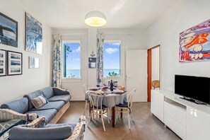 Un salon comprenant un canapé, une table à manger, des chaises, un téléviseur et des œuvres d’art accrochées aux murs.
