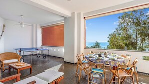 Una stanza con un tavolo da ping pong, un tavolo da pranzo con sedie, un divano e un'ampia finestra con vista.