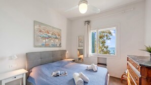 Una camera da letto con un letto, una scrivania, una cassettiera, un ventilatore a soffitto e una finestra con vista.