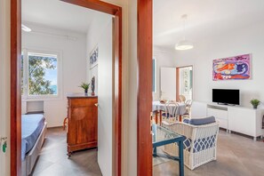 Une pièce comprenant un lit, une armoire en bois, une table à manger, une chaise en osier, un téléviseur et des œuvres d’art accrochées au mur.