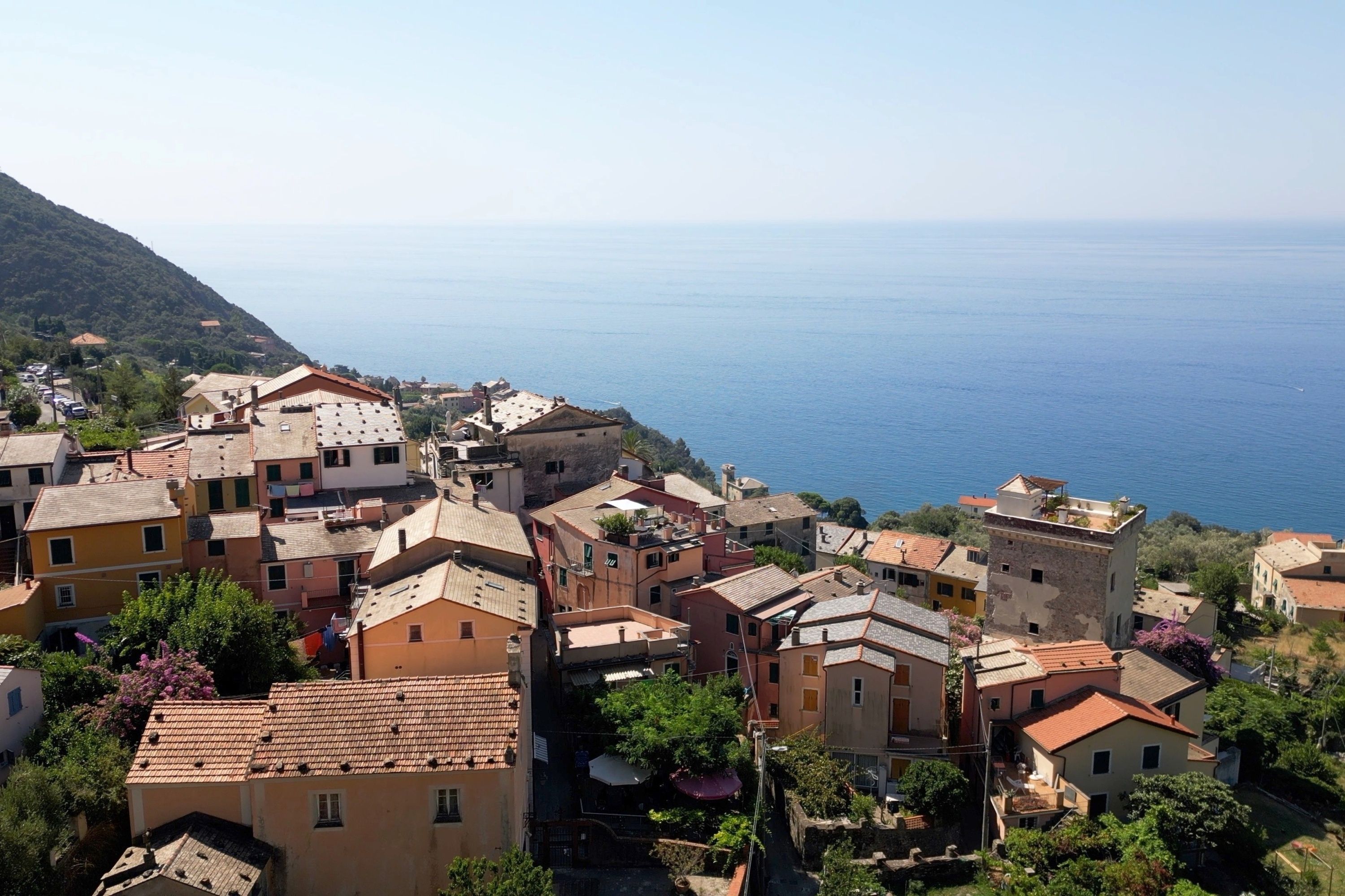 Un village côtier aux bâtiments aux toits de tuiles rouges, offrant une vue dégagée sur la mer et s’étendant sur un paysage vallonné.