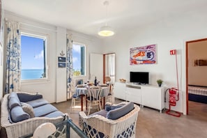A room with wicker furniture, a dining table, a television, and a fire extinguisher. - Appartamento Nel Verde Due Passi Dal Mare (Framura)