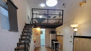 Ein kompakter Raum mit Etagenbett, Treppe, Küchenzeile und einem Gang zu einem weiteren Zimmer.