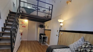 Ein Zimmer mit Etagenbett, Schreibtisch, Stuhl, Lampe und einer Treppe.