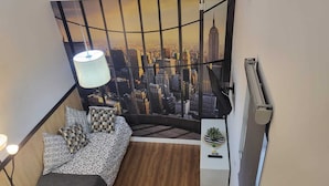 Ein Schlafzimmer mit Blick auf die Stadt, ein Bett mit gemusterten Betttextilien, eine Nachttischlampe und eine kleine Pflanze auf einem Nachttisch.