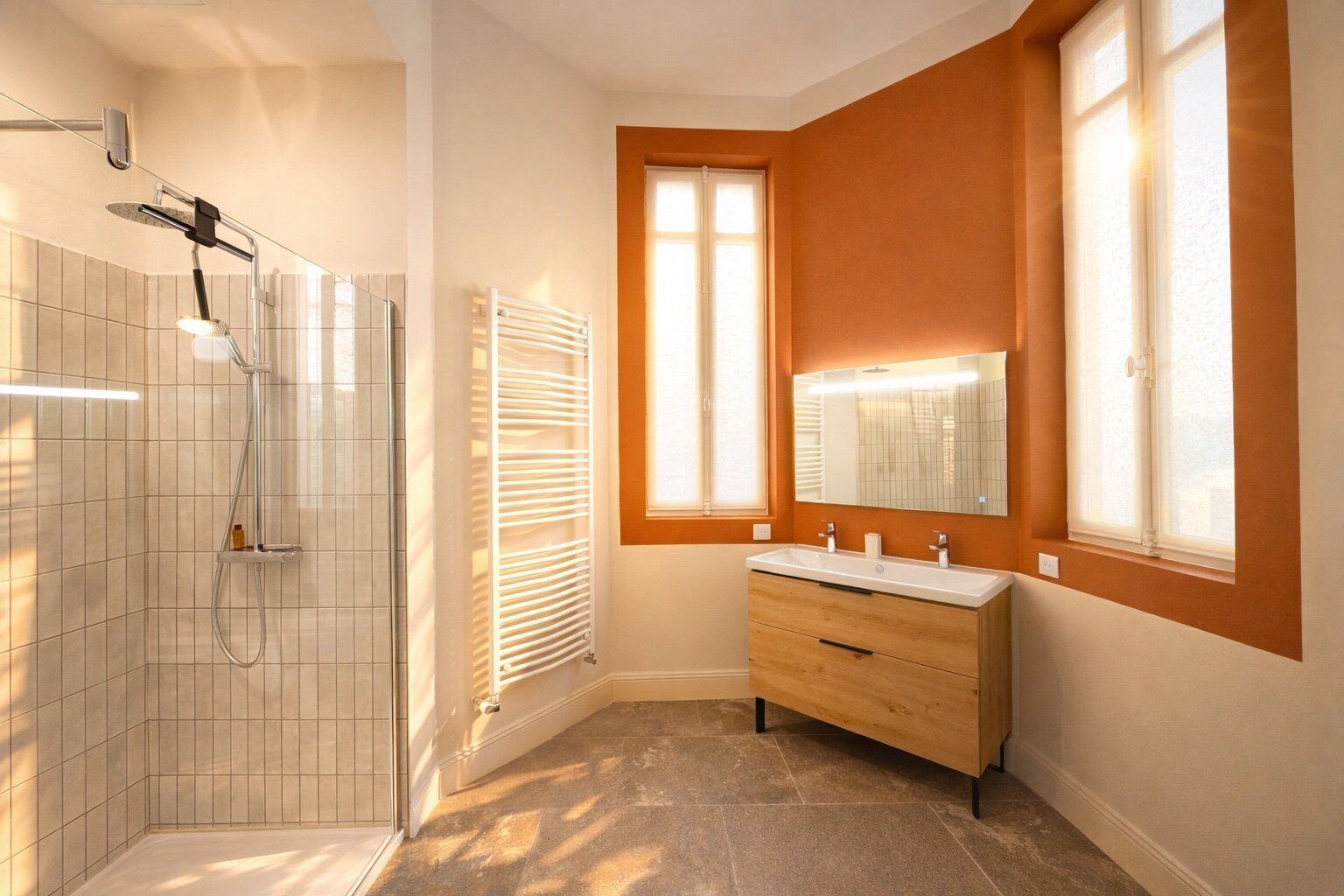 Une salle de bain avec une douche, un meuble-lavabo avec un miroir et une fenêtre qui laisse entrer la lumière naturelle.