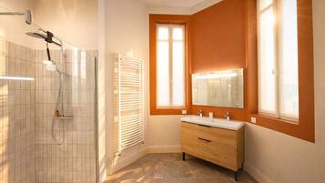 Une salle de bain avec une douche, un meuble-lavabo avec un miroir et une fenêtre qui laisse entrer la lumière naturelle.