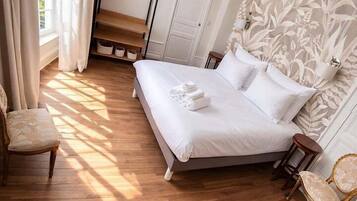 Une chambre à coucher avec un lit, un plancher en bois, un luminaire suspendu, une chaise et une fenêtre avec des rideaux.
