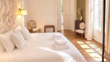 Une chambre spacieuse avec un grand lit, un luminaire suspendu et une vue sur l’extérieur par une fenêtre.