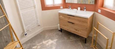 Un bagno con un mobile bagno in legno, uno specchio, una finestra e un termosifone.