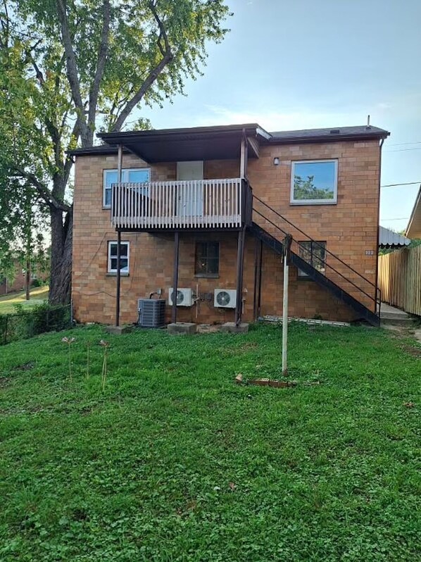 A two-story brick house with a balcony, air conditioning units, and a staircase leading to the upper floor.