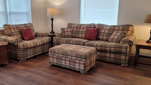 A living room with a sectional sofa, ottoman, two side tables with lamps, and a wooden cabinet. - Top-Floor Duplex Near Marshall University (Huntington)