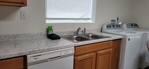 A kitchen with a marble countertop, a dishwasher, a sink, a window with blinds, and a washing machine.