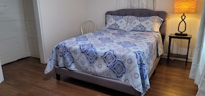 A bed with a patterned bedspread, a bedside table with a lamp, and a chair.