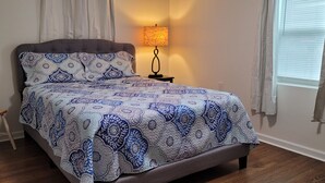 A bed with patterned bedding, a bedside lamp, a chair, and a window with curtains. - Top-Floor Duplex Near Marshall University (Huntington)