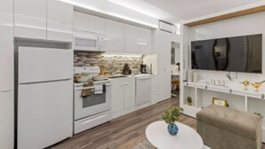 A modern kitchen with white cabinetry, a built-in oven, and a microwave. There is a dining area with a round table and a chair. - Sleeps 3 | Cleveland Clinic + University Circle (Cleveland)