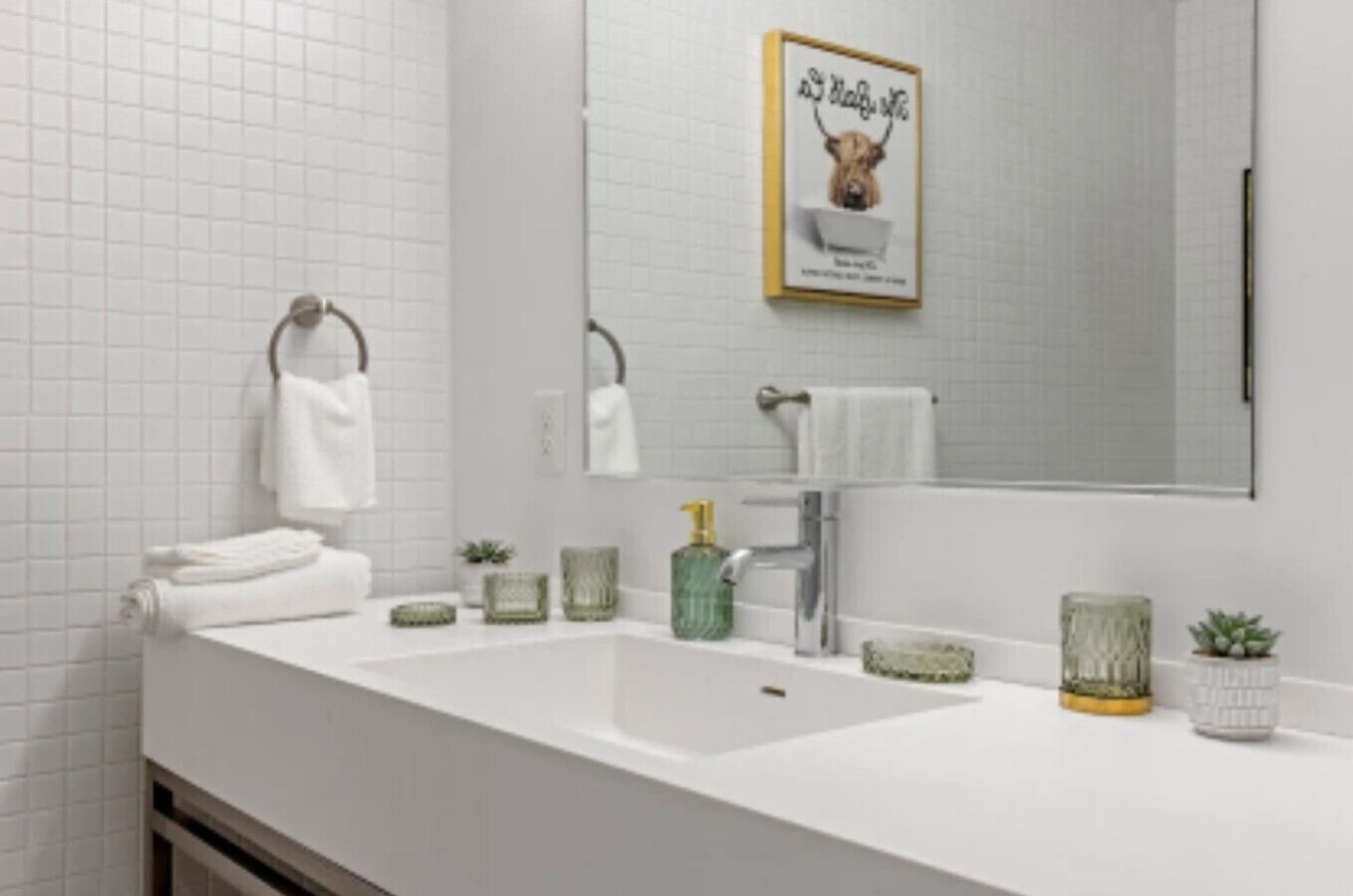 A bathroom with a white sink, two towel rings, a mirror, and a framed picture on the wall.