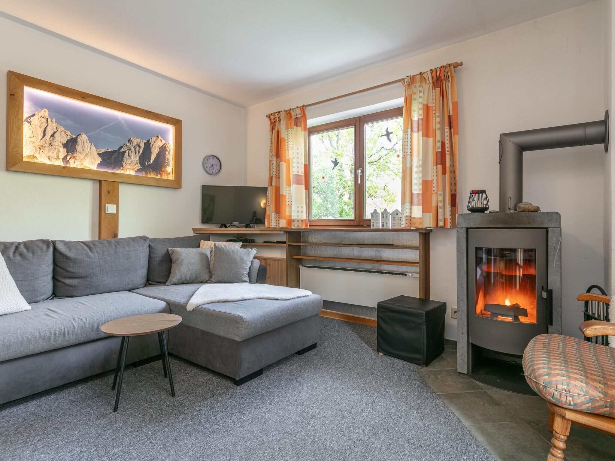 Ett modernt vardagsrum med en soffa, ett litet bord, en tv, en öppen spis och ett fönster med gardiner.
