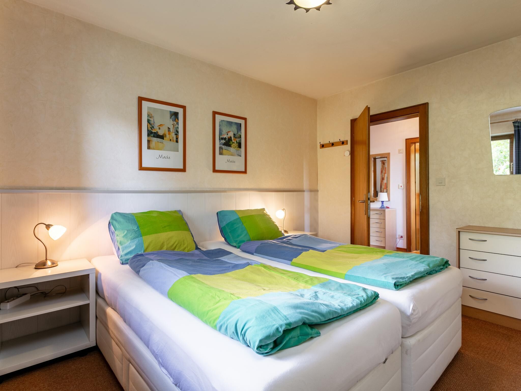 Een slaapkamer met twee bedden, nachtkastjes, een kaptafel en ingekaderde foto’s aan de muur.