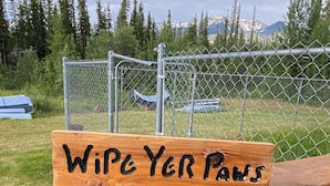A wooden sign with the text 'Wipe Yer Paws' on a wooden railing.