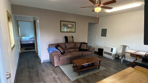 A living room with a brown sofa, a wooden coffee table, a ceiling fan, and a flat-screen TV.