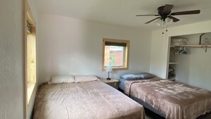 A room with two beds, a ceiling fan, a window, and a small table with a lamp.