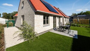 A house with a sloped red roof, solar panels, a patio with chairs, and a well-maintained lawn. - Two holiday homes located next to each other. (Koksijde)