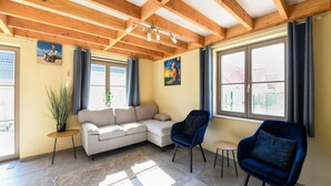 A living room with a wooden ceiling, a sofa, two armchairs, a small table, and a potted plant. - Two holiday homes located next to each other. (Koksijde)