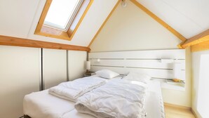 A bedroom with a sloped ceiling, a skylight, a bed with white bedding, a bedside table, and a nightstand. - Two holiday homes located next to each other. (Koksijde)
