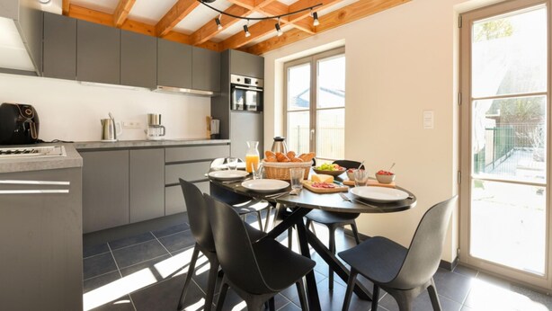 A modern kitchen with grey cabinets, a dining table with chairs, and a large window. - Two holiday homes located next to each other. (Koksijde)