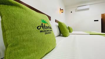 Quarto de hotel com cama, almofadas verdes, cabeceira, luminária fixada na parede e unidade de ar condicionado.