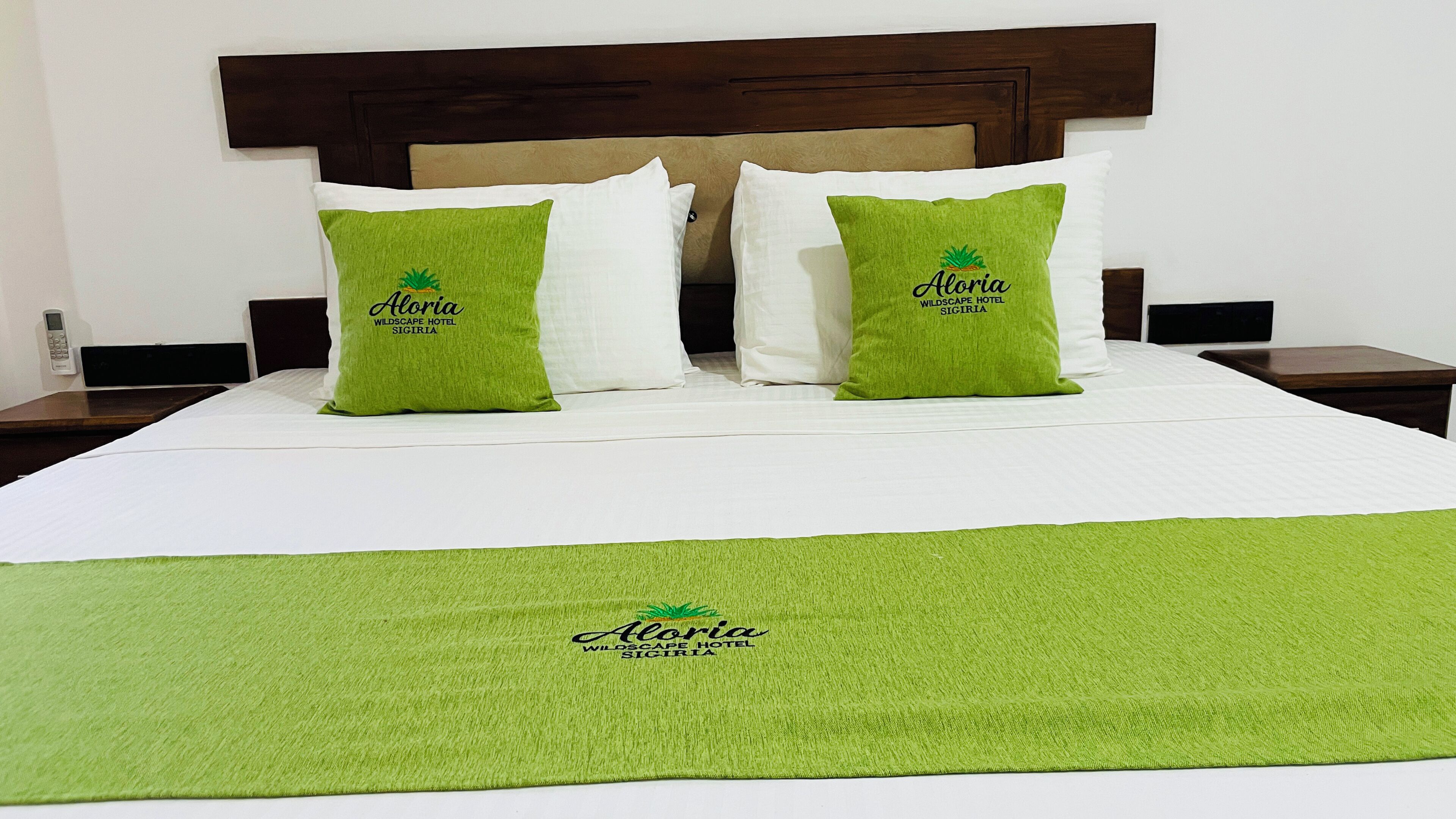Quarto de hotel com uma cama, duas almofadas verdes com a inscrição 'Aloria Wildscape Hotel Sigria' e um espalha cama branco, além de um cobertor verde.