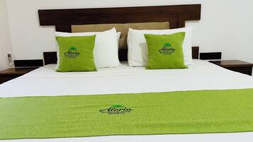 Quarto de hotel com uma cama, duas almofadas verdes com a inscrição 'Aloria Wildscape Hotel Sigria' e um espalha cama branco, além de um cobertor verde.