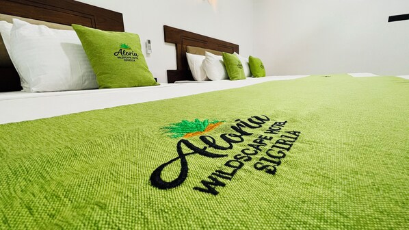 A bed with green bedding and pillows, a headboard, and a wall-mounted control panel. - Aloria Sigiriya (Sigiriya)