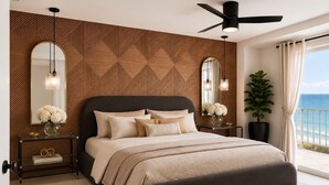 Une chambre à coucher avec un lit, des tables de chevet, un miroir, un ventilateur de plafond et une vue sur l’océan.