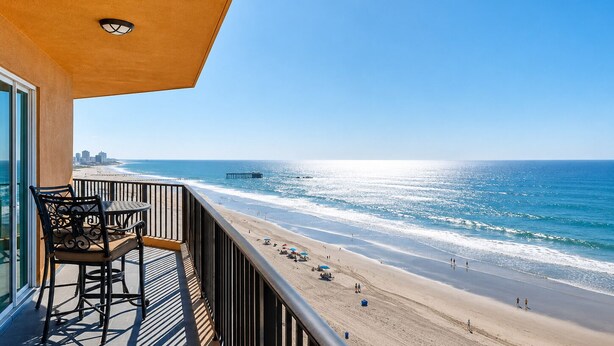 Un balcon donnant sur une plage et l’océan, une table avec des chaises et une balustrade.