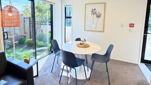 Una habitación moderna con una mesa redonda, cuatro sillas, un sofá y ventanas amplias que dan a vistas del exterior.