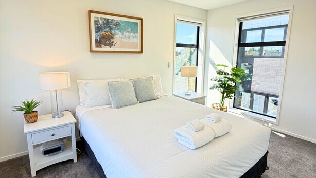 Un dormitorio ordenado con cama, mesita de noche, lámpara y un cuadro en la pared.